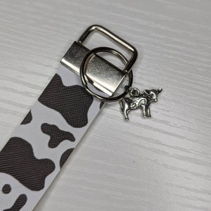 May include: A black and white cow print keyring with a silver key ring and a silver cow charm.