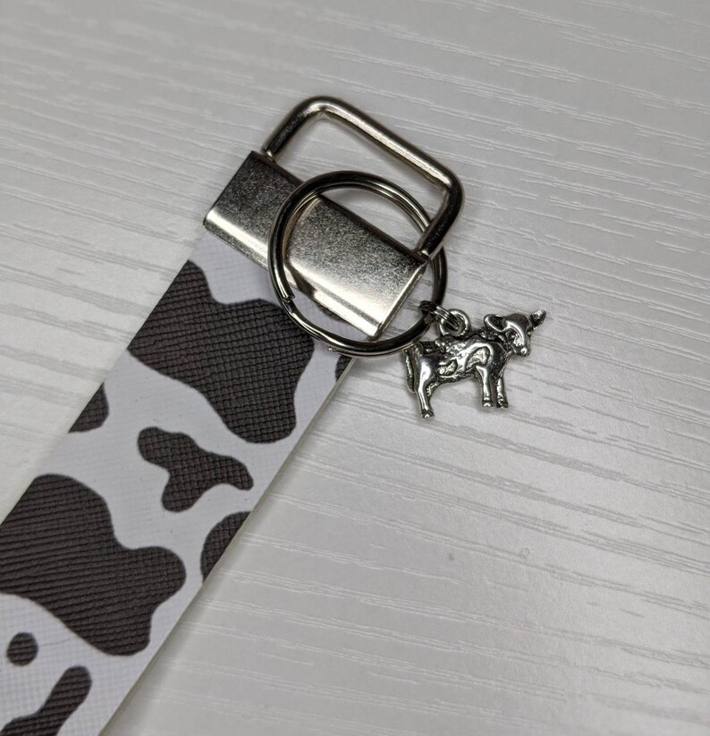 May include: A black and white cow print keyring with a silver key ring and a silver cow charm.