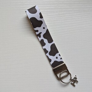 May include: A black and white cow print key chain with a silver key ring and a small silver cow charm.