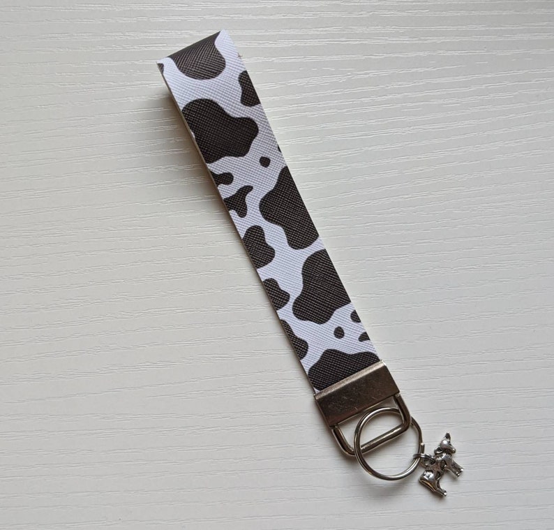 May include: A black and white cow print key chain with a silver key ring and a small silver cow charm.