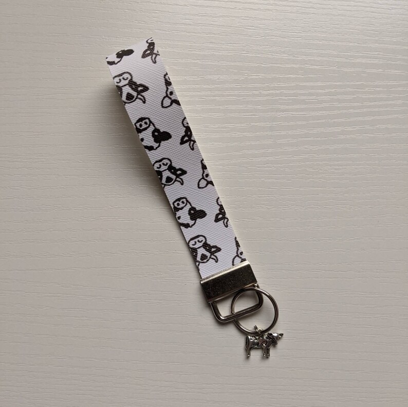 May include: White and black cow print keyring with a silver cow charm.