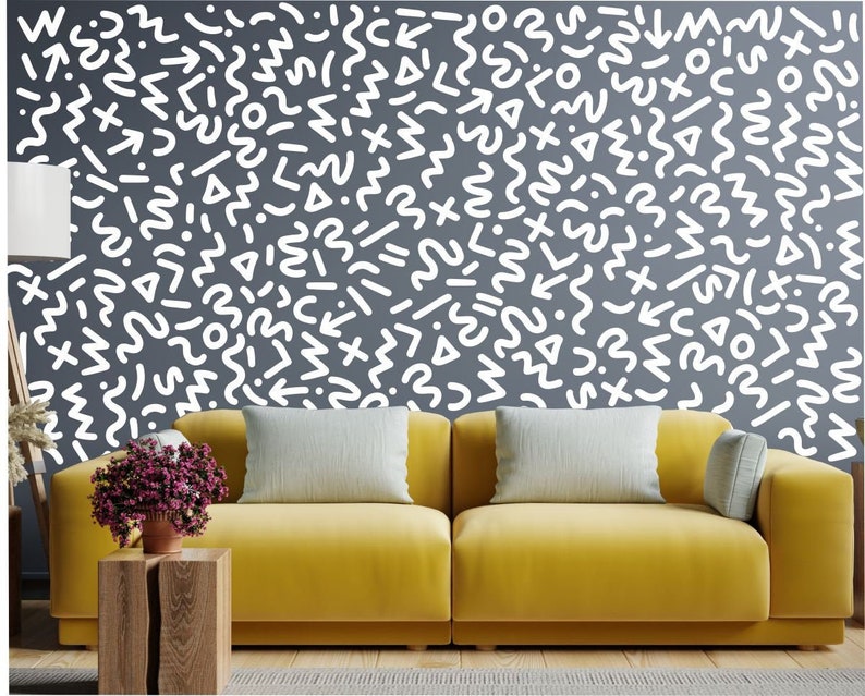 May include: A yellow sofa with two white throw pillows in front of a wall with a white geometric pattern. The pattern is made up of various shapes, including circles, squares, triangles, and wavy lines.