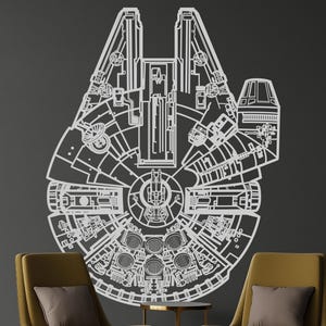 Può includere: Un grande schema bianco dell'astronave Millennium Falcon è montato su un muro grigio scuro. Il design dettagliato mostra l'esterno e i componenti interni della nave. Due poltrone gialle e un tavolino sono di fronte al muro.