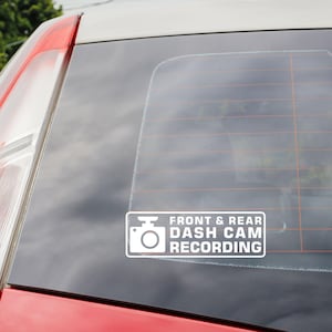 Puede incluir: Pegatina blanca en la ventana de un coche que dice "Front & Rear Dash Cam Recording". La pegatina tiene un icono de cámara blanco.