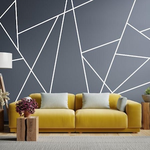 Peut inclure: Salon moderne avec un canapé jaune et des coussins clairs, devant un mur gris avec des lignes géométriques blanches. Tables d'appoint en bois avec plantes et lampe.