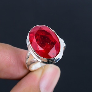 Peut inclure: Bague en argent ornée d'une grande pierre rouge ovale et facettée. La pierre est sertie dans un anneau en argent poli, créant un contraste saisissant. Le design de la bague est simple mais élégant, mettant en valeur la couleur vibrante et la brillance de la pierre.