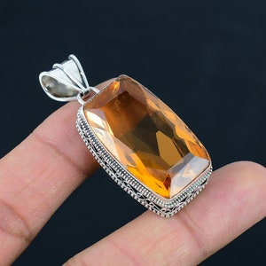 May include: A silver pendant with a large, rectangular, orange topaz gemstone. The pendant has a detailed, ornate silver border.