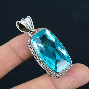 May include: A silver pendant with a large, rectangular, light blue gemstone. The gemstone is faceted and has a high polish. The pendant has a detailed, ornate silver frame.