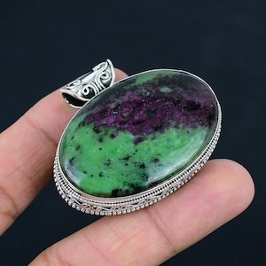 May include: Oval green and purple gemstone pendant with silver filigree design. The pendant is set in a silver bezel and has a silver bail.