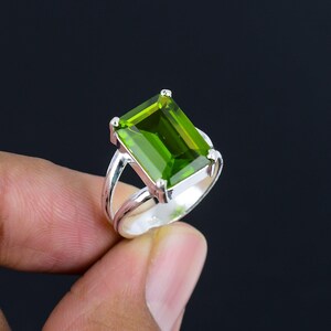 May include: A silver ring with a large, emerald green gemstone. The gemstone is cut in a rectangular shape with beveled edges.