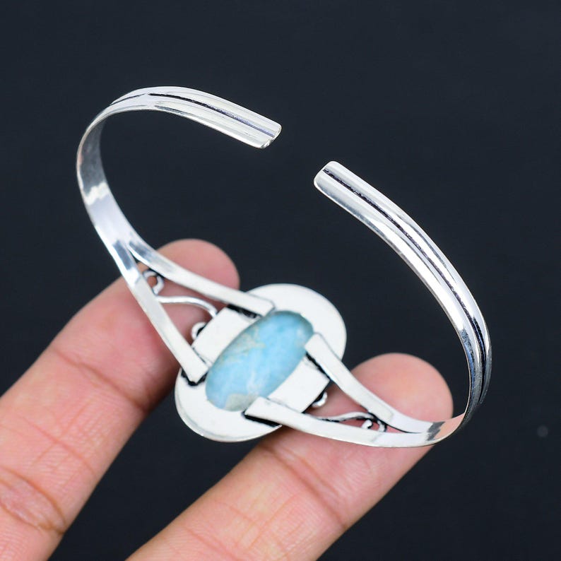 May include: Silver bangle bracelet with a light blue oval gemstone set in a silver filigree design.