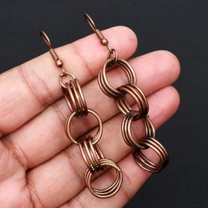 May include: A pair of drop earrings featuring a chain-link design made of antiqued copper-toned metal. Each earring consists of three interconnected circular rings that hang vertically from a standard hook-style ear wire closure.