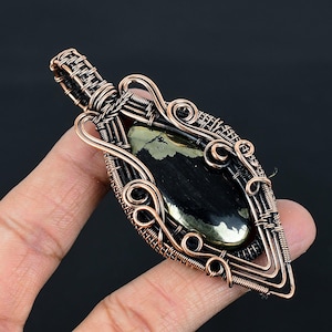 May include: A copper wire wrapped pendant featuring a black and gold gemstone. The pendant is shaped like a teardrop and has intricate wirework details.