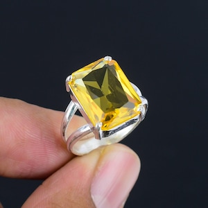 May include: A silver ring featuring a large, rectangular, faceted yellow gemstone set in a four-prong mount. The band consists of two thin, parallel silver wires that meet at the base of the setting, creating a simple and open design structure.