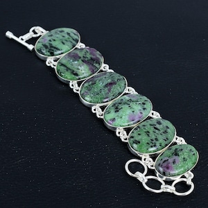 Pode incluir: Uma pulseira de prata com sete pedras ovais de cor verde e rosa. A pulseira tem um fecho.