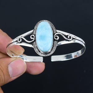 May include: A silver bangle bracelet with a light blue oval gemstone set in a silver filigree design.