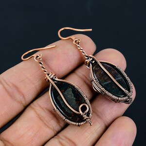 May include: A pair of copper wire wrapped earrings with green and brown jasper stone accents.