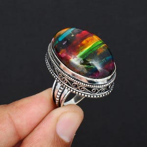 May include: A silver ring with a large oval-shaped gemstone. The gemstone is a mix of iridescent colors, including red, orange, yellow, green, blue, and purple.