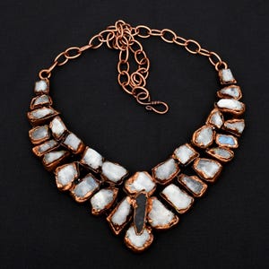 Puede incluir: Un collar de cadena de cobre con una pieza grande y llamativa hecha de cristales de piedra lunar blanca. Los cristales tienen una forma irregular y un aspecto natural y bruto. El collar es una pieza de joyería única y llamativa.