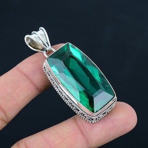 Puede incluir: Un colgante de plata con una gran piedra rectangular de color verde esmeralda engastada en un marco de plata decorativo.
