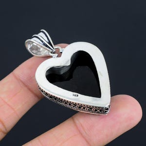 May include: Silver heart-shaped pendant with an intricate filigree design. The pendant has a black stone in the center and is marked "925" on the back.
