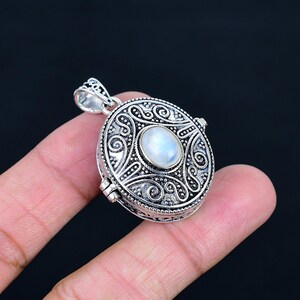 May include: A round silver locket pendant featuring an oval moonstone cabochon at the centre. The metal surface is decorated with intricate oxidised scrollwork and granulated bead detailing, complete with a decorative silver bail at the top.