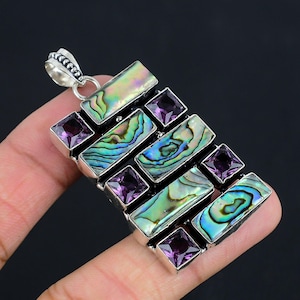 May include: A rectangular pendant featuring four iridescent abalone shell inlays arranged in a staggered pattern, interspersed with four square-cut purple amethyst gemstones. The stones are set in a silver-toned metal frame with a decorative bail.