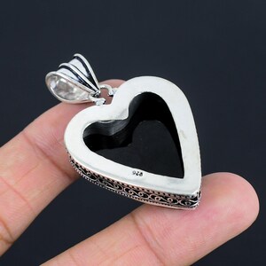 May include: Silver heart-shaped pendant with an intricate filigree design. The pendant has a black stone in the center and is marked "925" on the back.