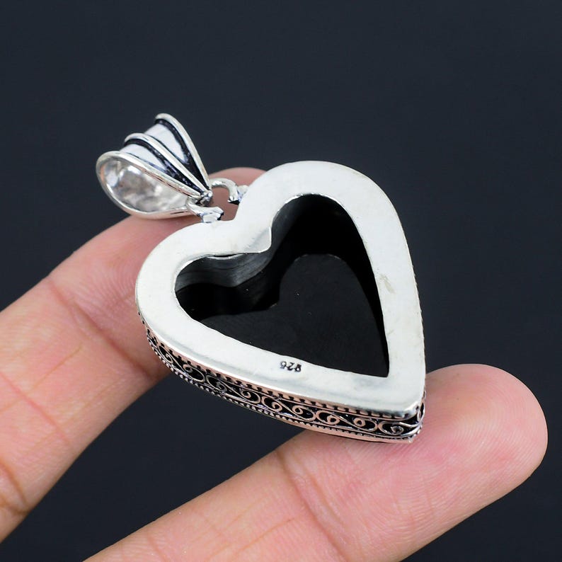 May include: Silver heart-shaped pendant with an intricate filigree design. The pendant has a black stone in the center and is marked "925" on the back.