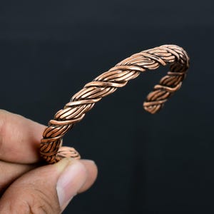 May include: A copper bracelet with a braided design. The bracelet is open and adjustable.