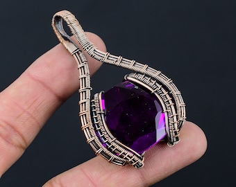 Può includere: Un ciondolo con una pietra preziosa viola con un design in filo di rame avvolto. Il ciondolo ha la forma di una lacrima e presenta un design delicato e intricato.