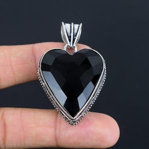 May include: A silver heart-shaped pendant with a black gemstone. The pendant has a detailed silver border.