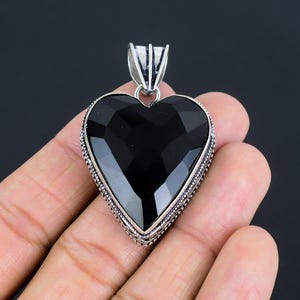 May include: A black onyx heart pendant with a silver ornate border. The pendant is on a black background.