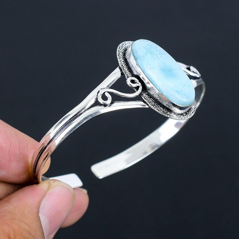May include: A silver bangle bracelet with a light blue oval gemstone set in a decorative silver frame.