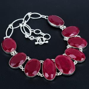 May include: A silver necklace with a chain and a row of oval-shaped red gemstones.