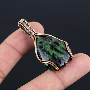 Peut inclure: Un pendentif en pierre précieuse verte et noire enveloppé de fil de cuivre. Le pendentif est en forme de larme et a une finition polie.