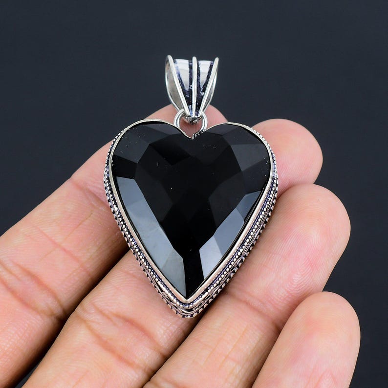 May include: A black heart-shaped pendant with a silver ornate border. The pendant is made of onyx and silver.
