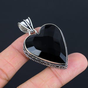 May include: A silver heart-shaped pendant with a black gemstone. The pendant has an ornate silver border.