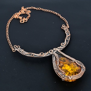 May include: A copper wire wrapped amber pendant necklace with a delicate, intricate design. The pendant is teardrop shaped and features a large amber stone.