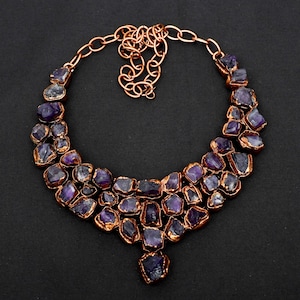 May include: A copper necklace with a cascading design of amethyst stones. The stones are irregularly shaped and have a deep purple color. The necklace has a simple chain closure.