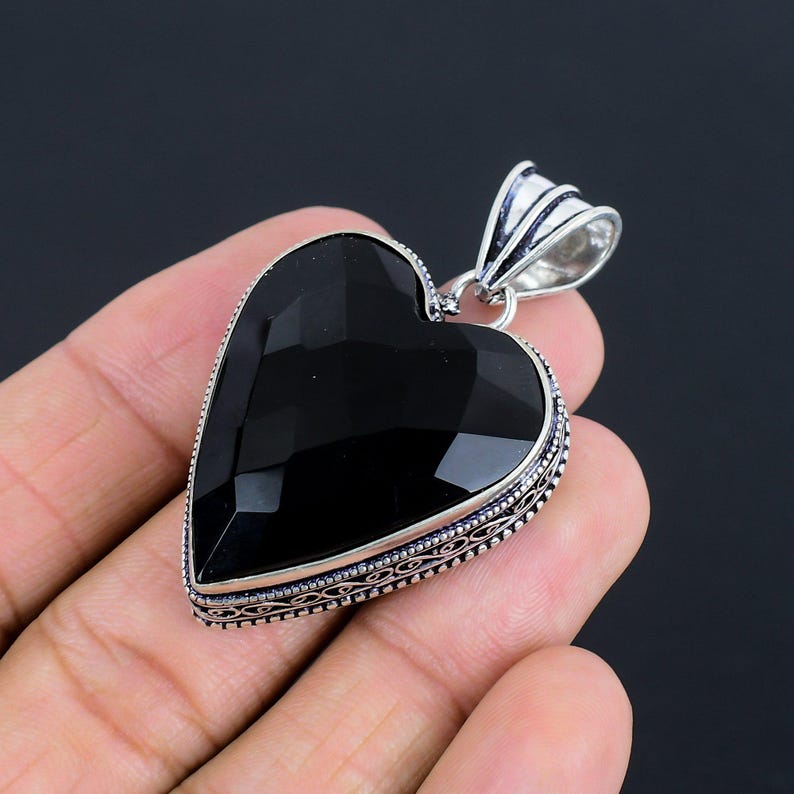 May include: A black onyx heart pendant with a silver filigree border. The pendant is hanging from a silver bail.