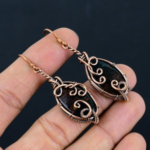 May include: A pair of copper wire wrapped earrings with a dark green and brown stone in the center of each earring.