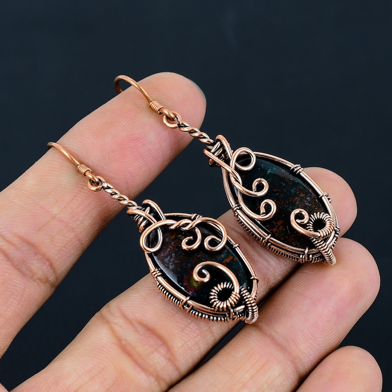 May include: A pair of copper wire wrapped earrings with a dark green and brown stone in the center of each earring.