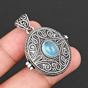 May include: An oval-shaped locket pendant crafted from oxidised silver-toned metal, featuring intricate scrollwork and beaded detailing. A smooth, translucent light blue cabochon stone is set in the centre, complemented by a decorative bail.