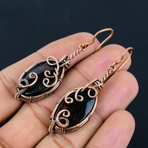 May include: A pair of copper wire wrapped earrings with a black and brown oval shaped stone. The earrings have a delicate, intricate design.