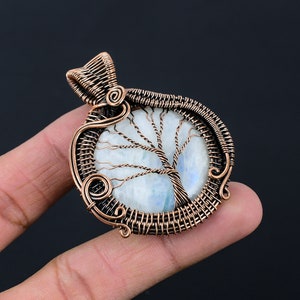May include: A copper wire wrapped pendant featuring a white moonstone with a tree of life design. The pendant is oval shaped and has a copper bail for hanging.