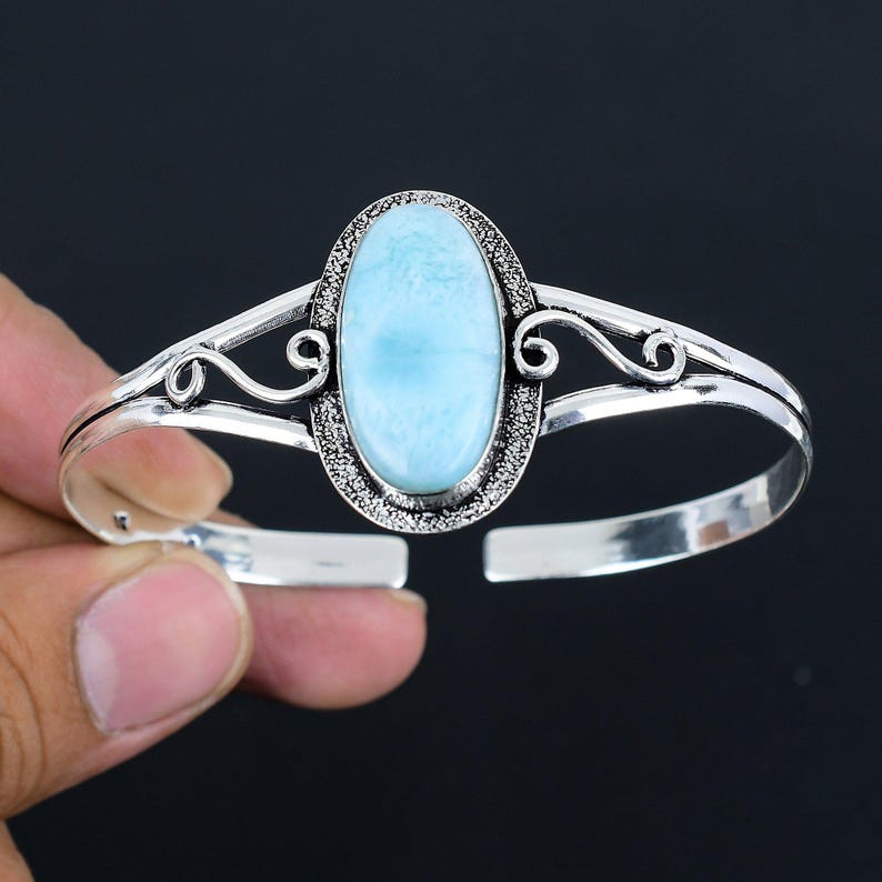 May include: A silver bangle bracelet with a light blue oval gemstone set in a silver filigree design.