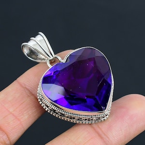 May include: A silver heart-shaped pendant with a large, faceted, purple amethyst gemstone. The pendant has a detailed silver border.