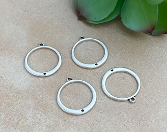 Könnte beinhalten: Vier silberfarbene runde Anhänger aus Metall mit einem kleinen Loch oben und einem kleineren Loch in der Mitte des Kreises.