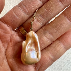 May include: A baroque pearl pendant necklace. The pendant is a large, irregularly shaped pearl with a creamy, iridescent surface. It hangs from a delicate gold chain with a small diamond accent.